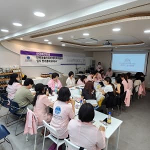 현수막이 걸린 강의실에서 분홍 앞치마를 입고 실습 중인 수강생들