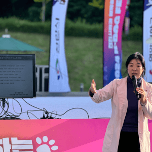 야외 행사장 배너 앞에서 마이크를 들고 설명하는 강연자